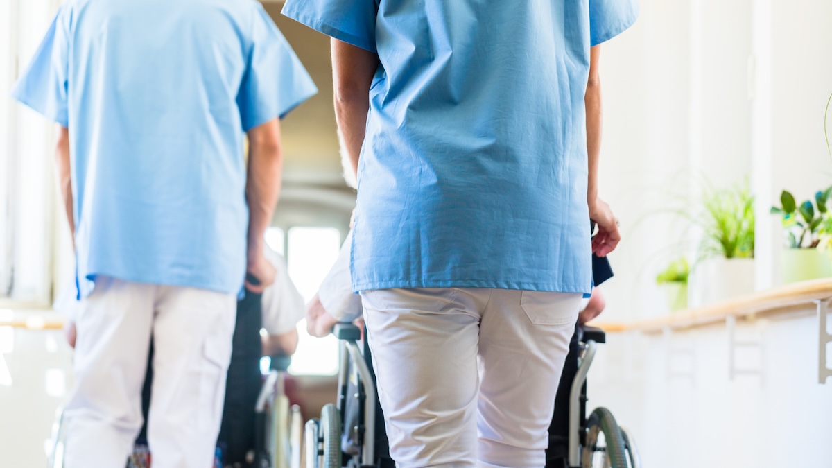 Symbolbild für Gehalt in der Pflege: Zwei Krankenschwestern schieben Rollstühle mit Patienten