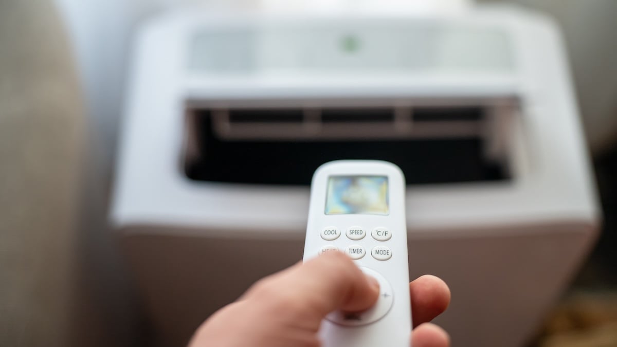 Jemand hält Fernbedienung vor mobile Klimaanlage
