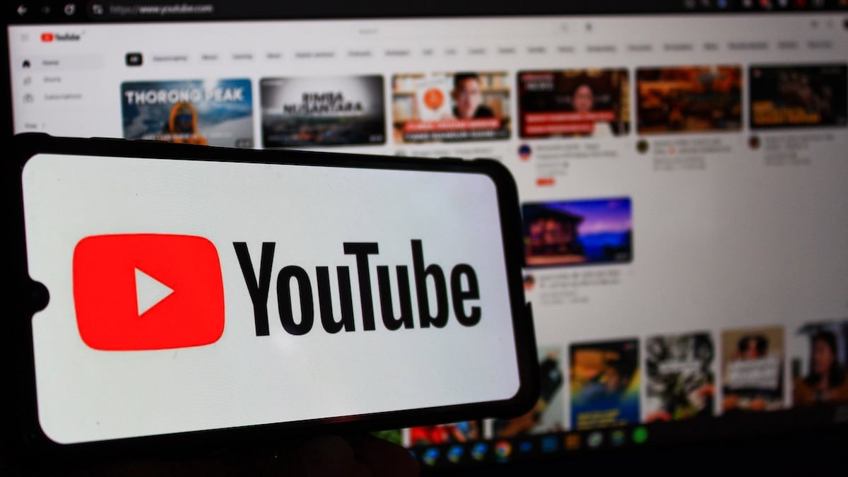 YouTube Logo und Schriftzug auf Smartphone vor Bild der Website