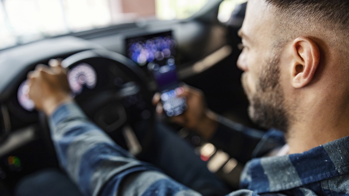 Mann fährt Auto, im Hintergrund sind Infotainment-Systeme zu sehen