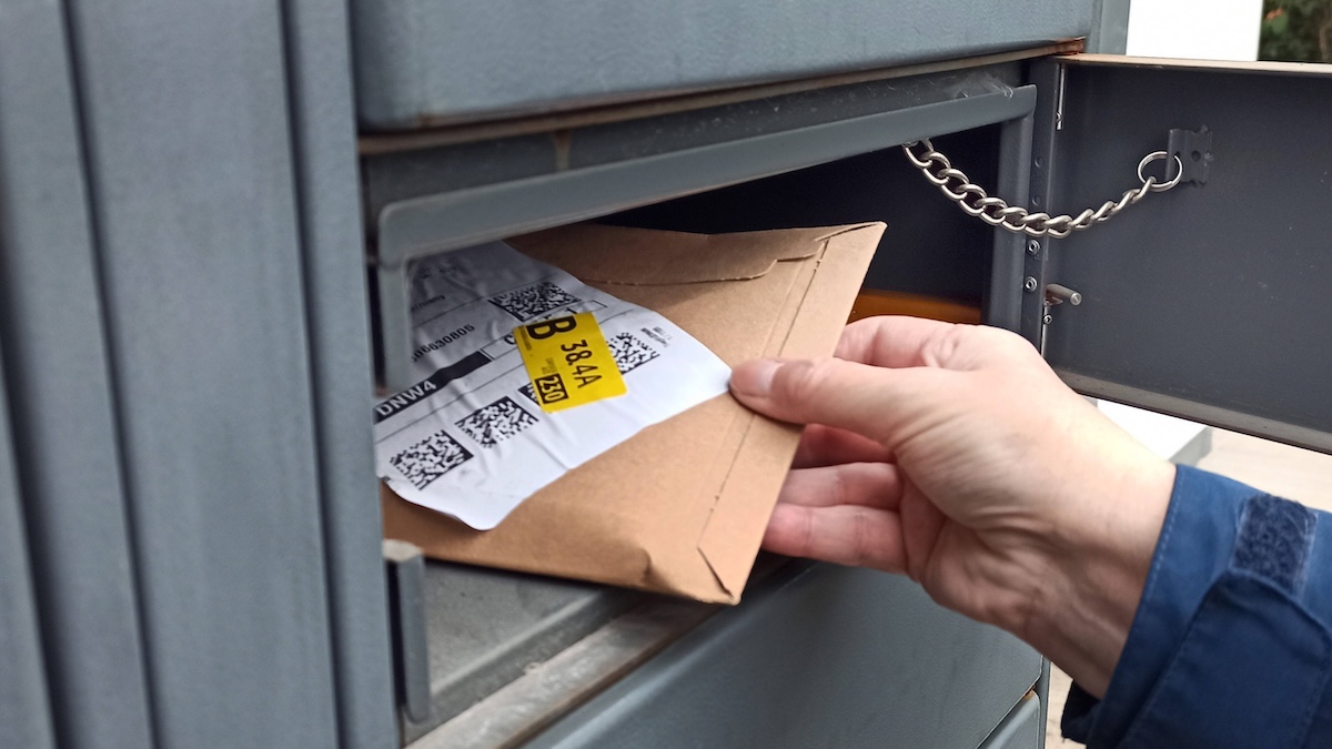 Was bedeuten die gelben Aufkleber auf Amazon-Päckchen? 2 Jemand nimmt ein kleines Amazon-Päckchen aus einer Paketstation, auf dem unter anderem ein kleiner gelber Aufkleber zu sehen ist