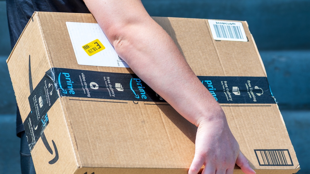 Paketzusteller trägt ein Amazon-Päckchen mit einem kleinen gelben Aufkleber unter dem Arm