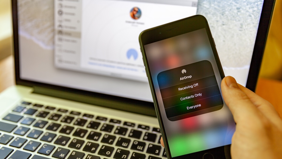 Smartphone mit Apple AirDrop, im Hintergrund ein MacBook