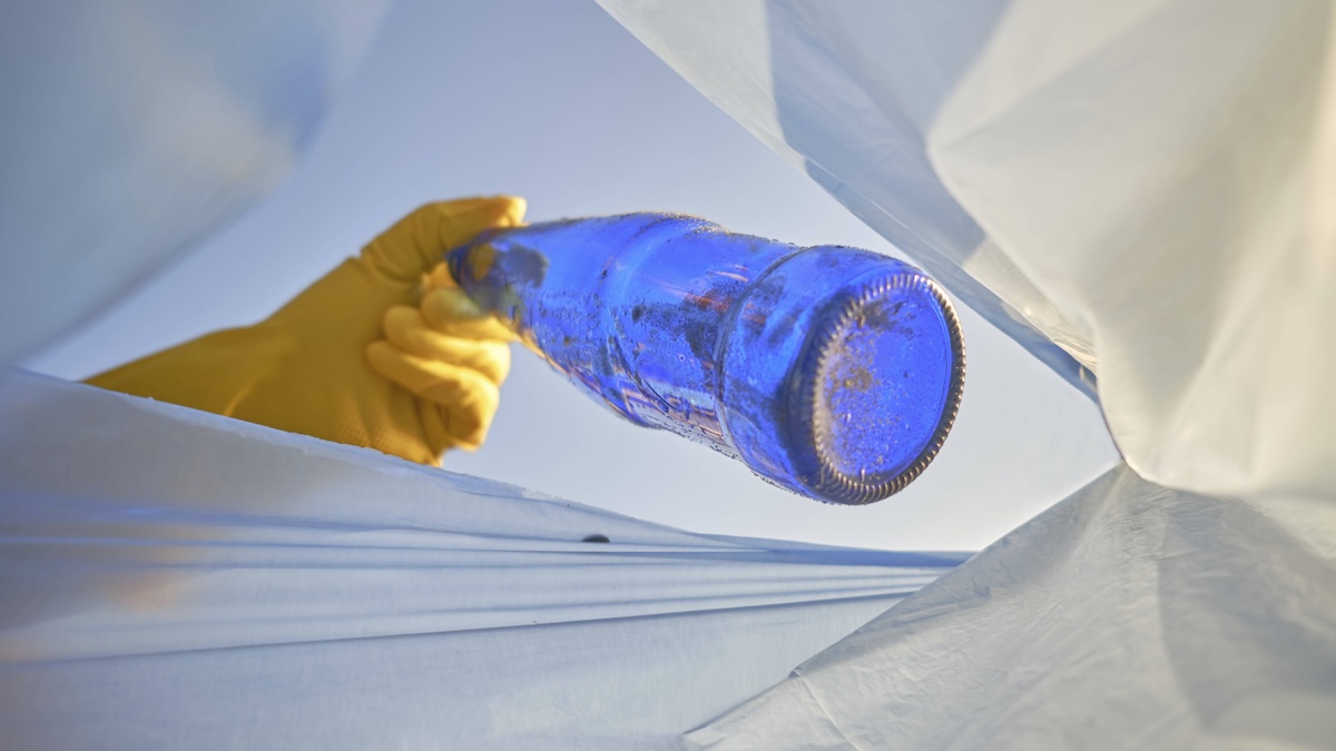 Jemand sammelt eine blaue Glasflasche auf