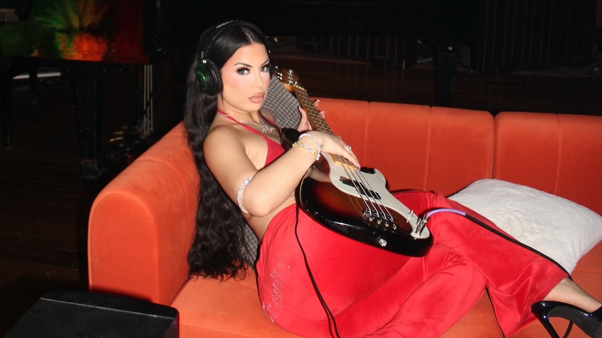 Bild der Sängerin Delarosa, die in einem roten Kleid mit einer Gitarre auf einem Sofa liegt