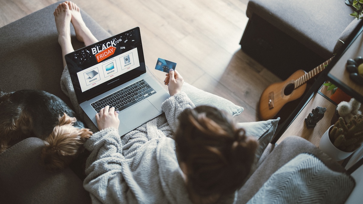 Warnung vor Fakeshops: Frau sitzt zum Black Friday beim Online-Shopping auf dem Sofa mit ihrem Laptop und hält eine Kreditkarte in der Hand