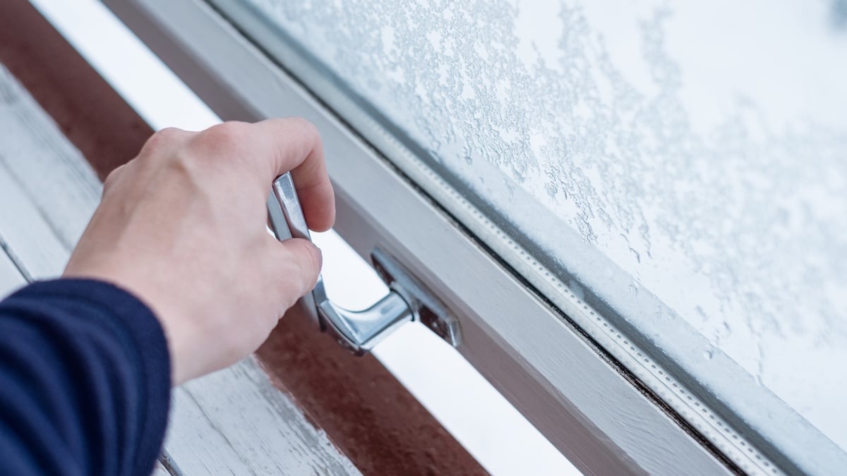 Doppel-Lüft-Technik: Wie man bei Kälte das Schlafzimmer richtig lüftet 10 Jemand öffnet ein Fenster mit Eiskristallen, um zu Lüften