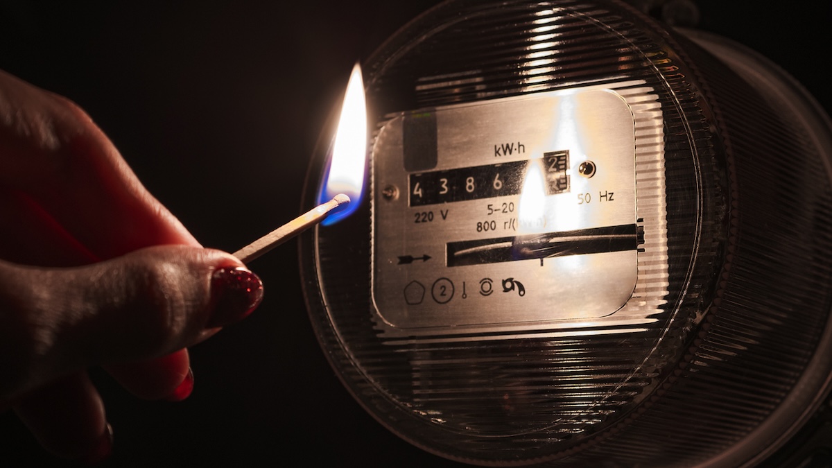 Frau hält bei Stromausfall ein brennendes Streichholz neben einen Stromzähler
