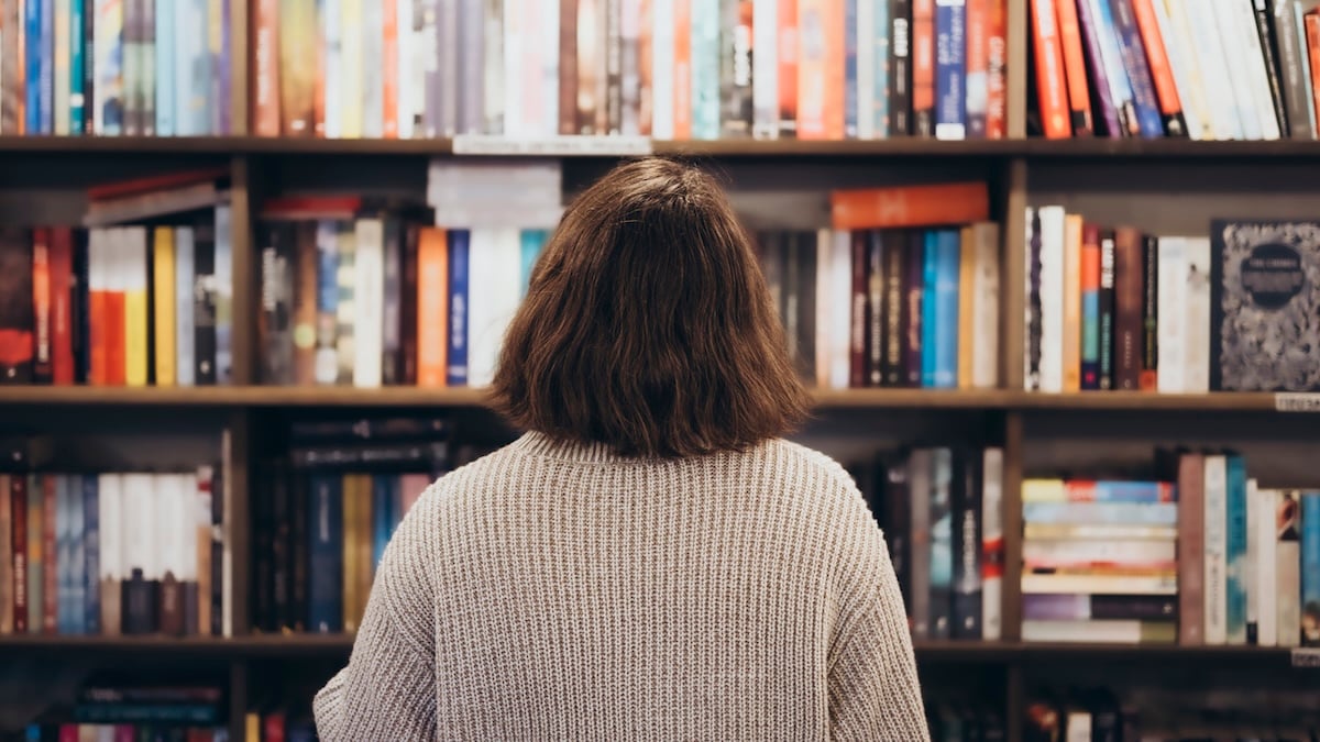 Wertvolle Bücher: Junge Frau steht mit dem Rücken zur Kamera, einem vollen Bücherregal zugewandt