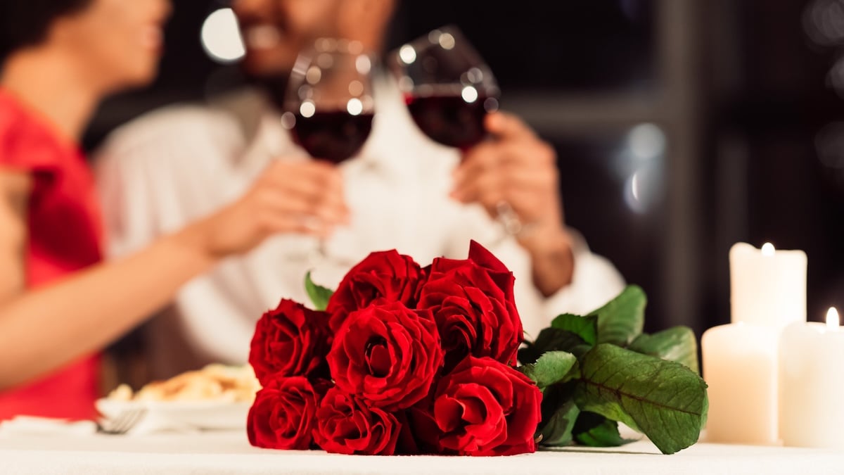 Dating-Trends 2026: Romantisches Date mt Rotwein-Gläsern und Rosenstrauß im Vordergrund und einem Pärchen im Hintergrund