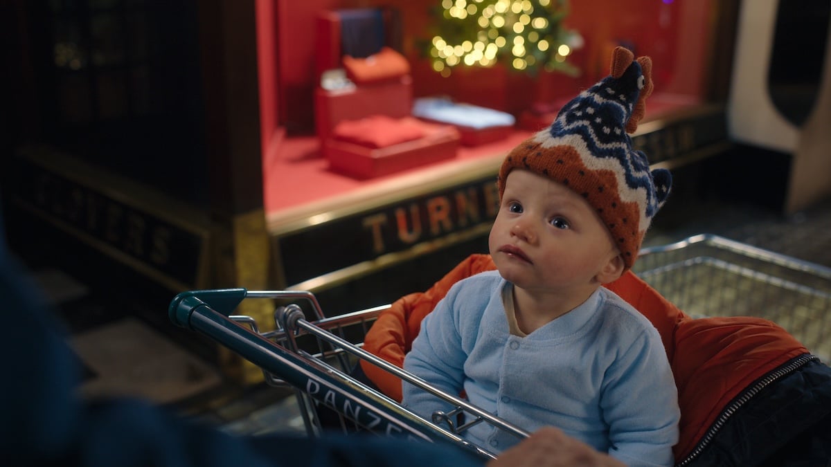 Szene aus der Netflix-Serie „Man vs Baby“, in der ein Baby mit Mütze in einem Einkaufswagen sitzt