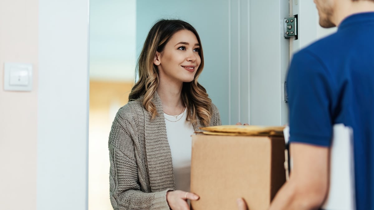 Frau nimmt lächelnd Pakete von einem Zusteller entgegen