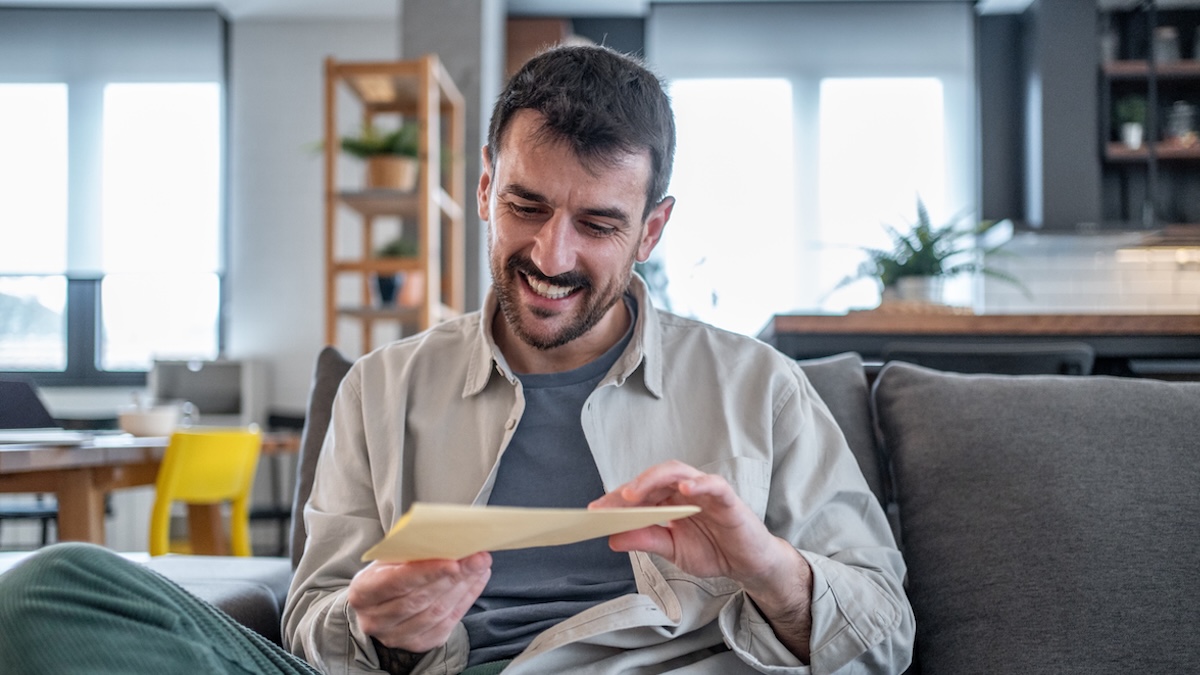 Österreich verschickt Bargeld per Post: Mann öffnet lächelnd einen Briefumschlag