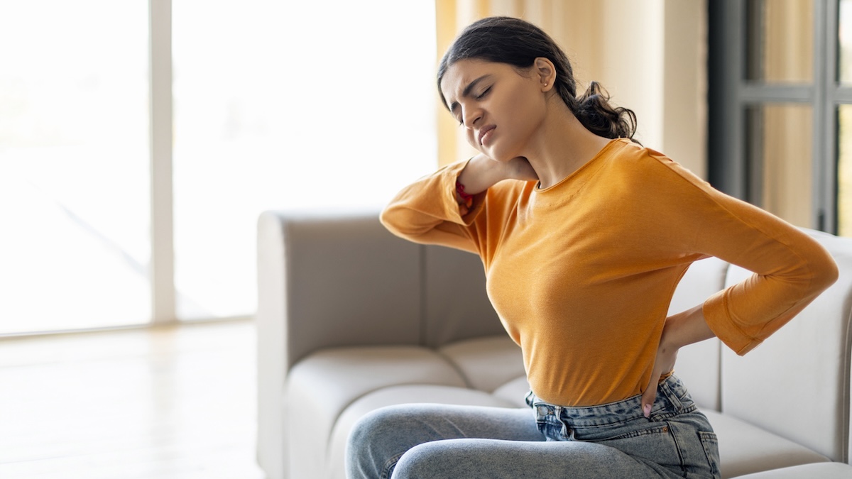 Versteckte Warnsignale: Wann man mit Rückenschmerzen unbedingt zum Arzt gehen sollte 11 Junge Frau mit Rückenschmerzen hält sich Nacken und Kreuz
