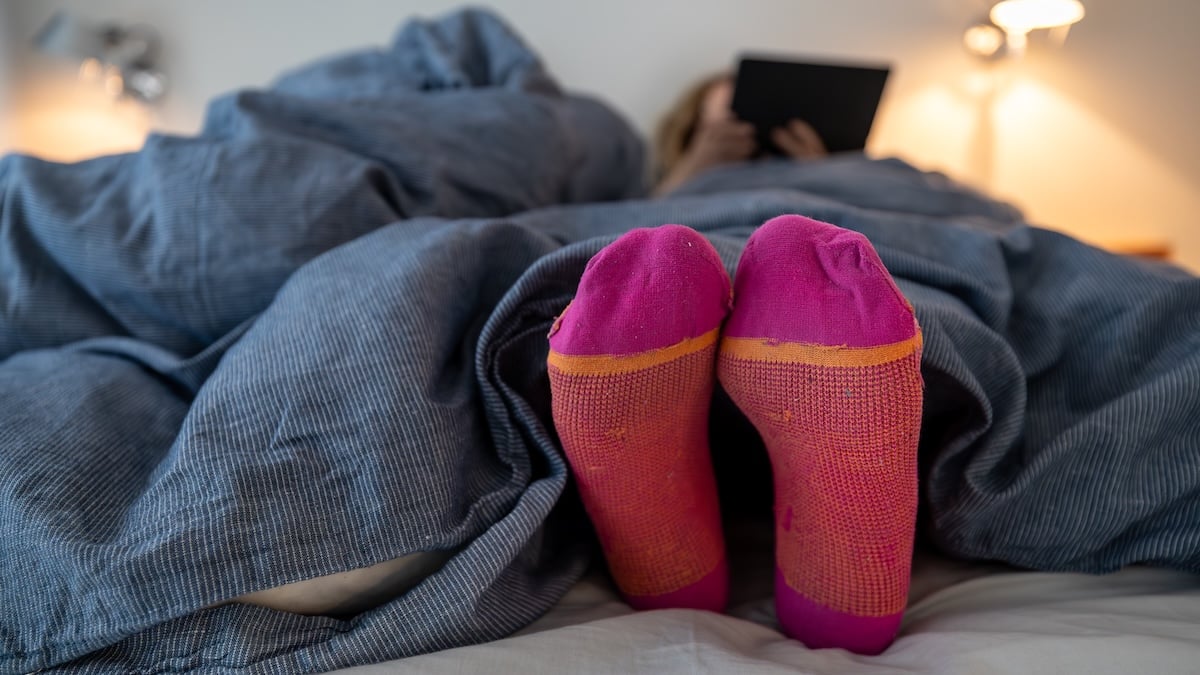 Socken im Bett an- oder ausziehen? Wissenschaft gibt klare Antwort 9 Frau trägt beim Lesen im Bett bunte Wollsocken
