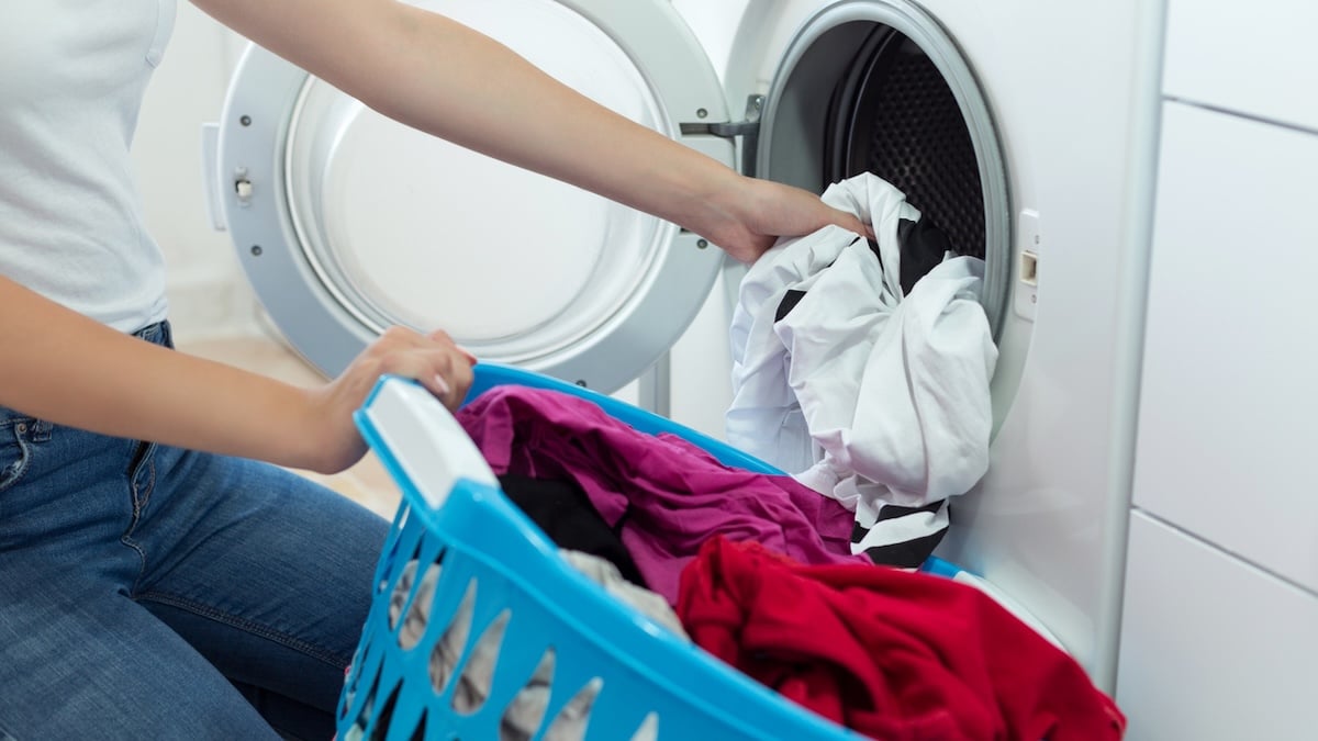 Frau steckt bunte Wäsche in eine Waschmaschine